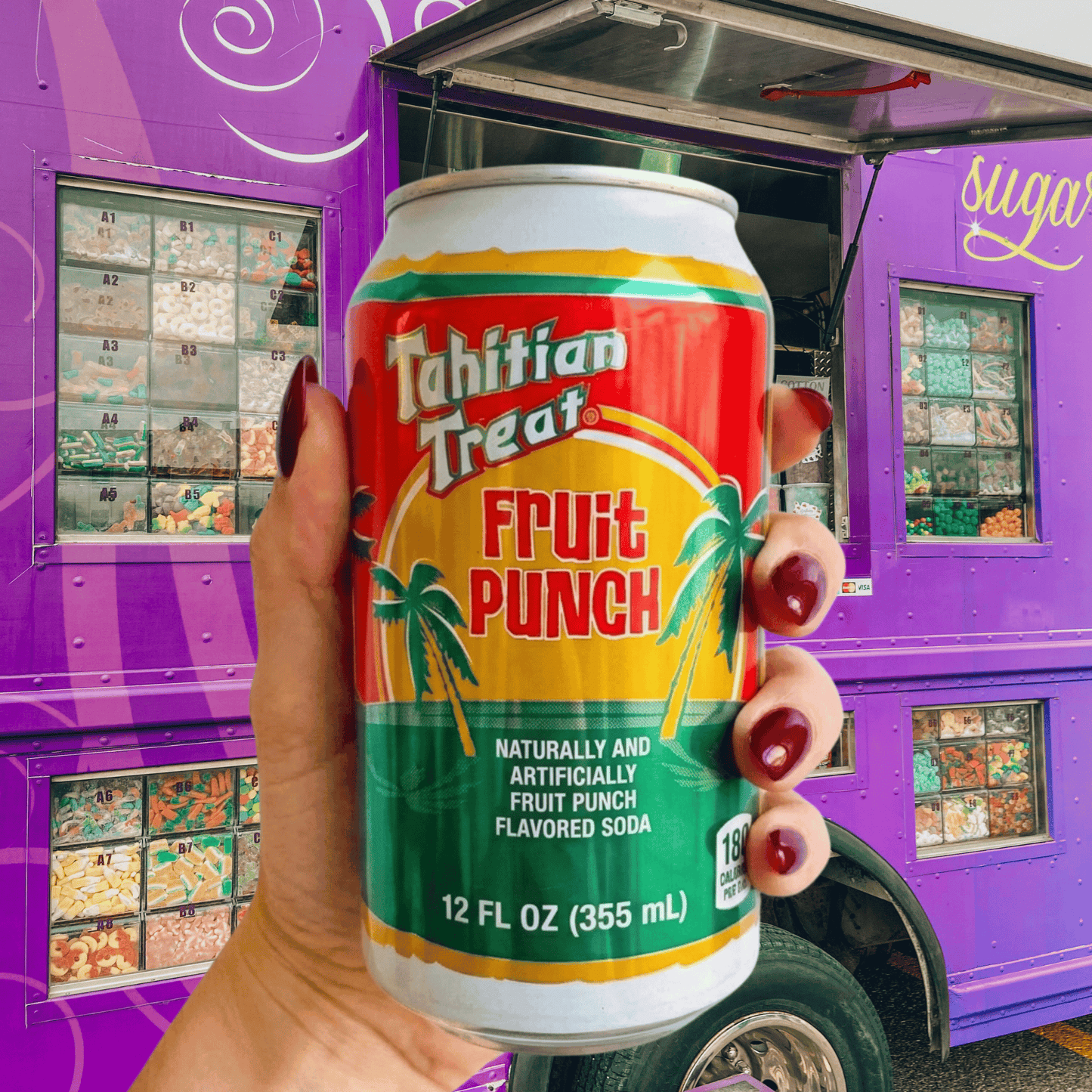 Hand holding a can of Tahitian Treat Fruit Punch soda in front of The Sugar Cube candy truck, highlighting the nostalgic drink featured in a story about candy, memories, and human connection.