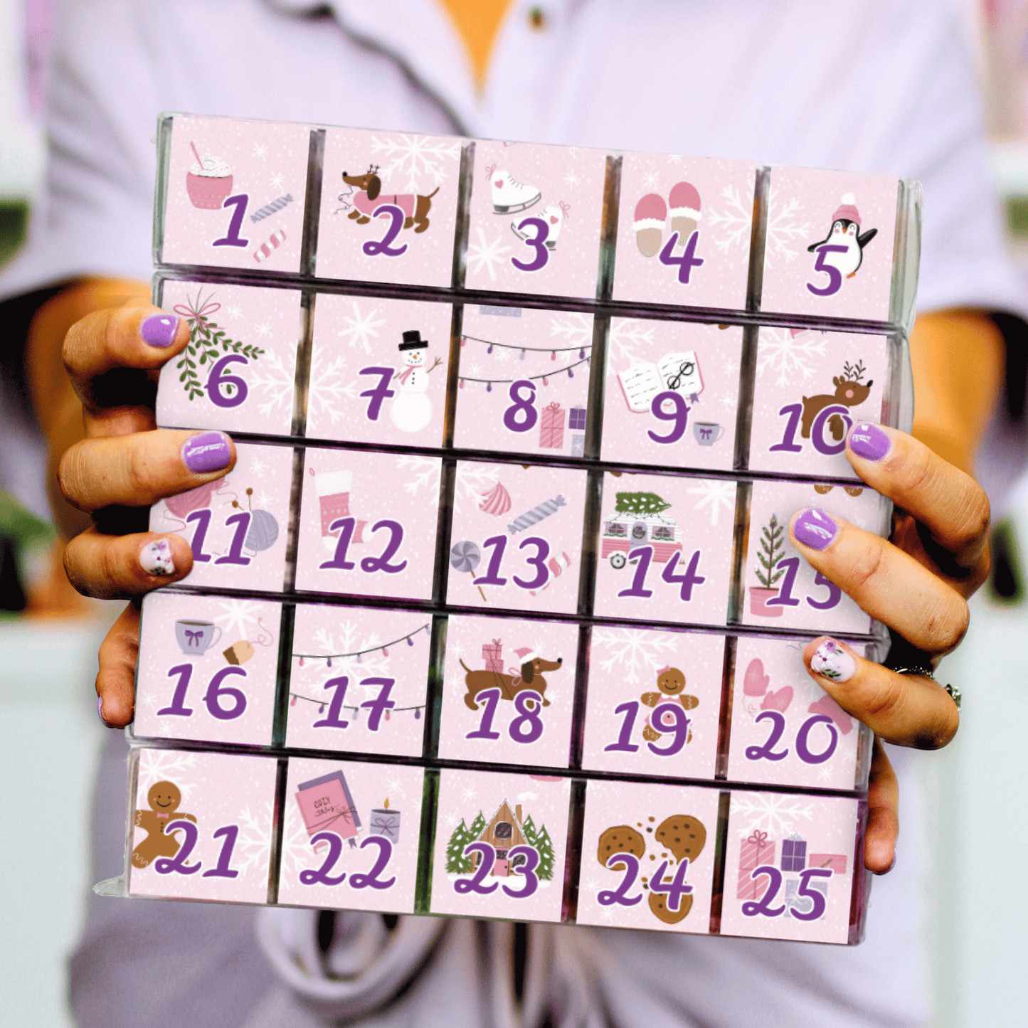 The Sugar Cube 2026 Individual Candy Advent Calendar held in two hands, featuring 25 numbered candy-filled cubes with pink holiday illustrations.