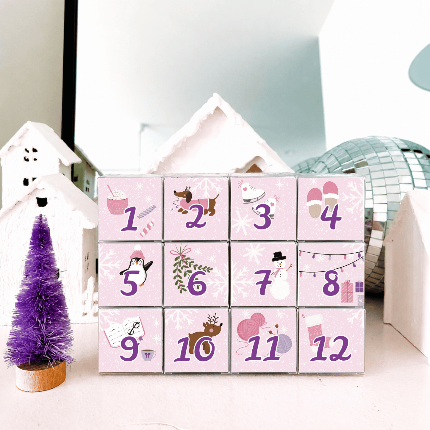 The Sugar Cube Individual 12-Day Candy Advent Calendar with 12 pink illustrated candy-filled cubes, styled with a purple Christmas tree and winter decorations.