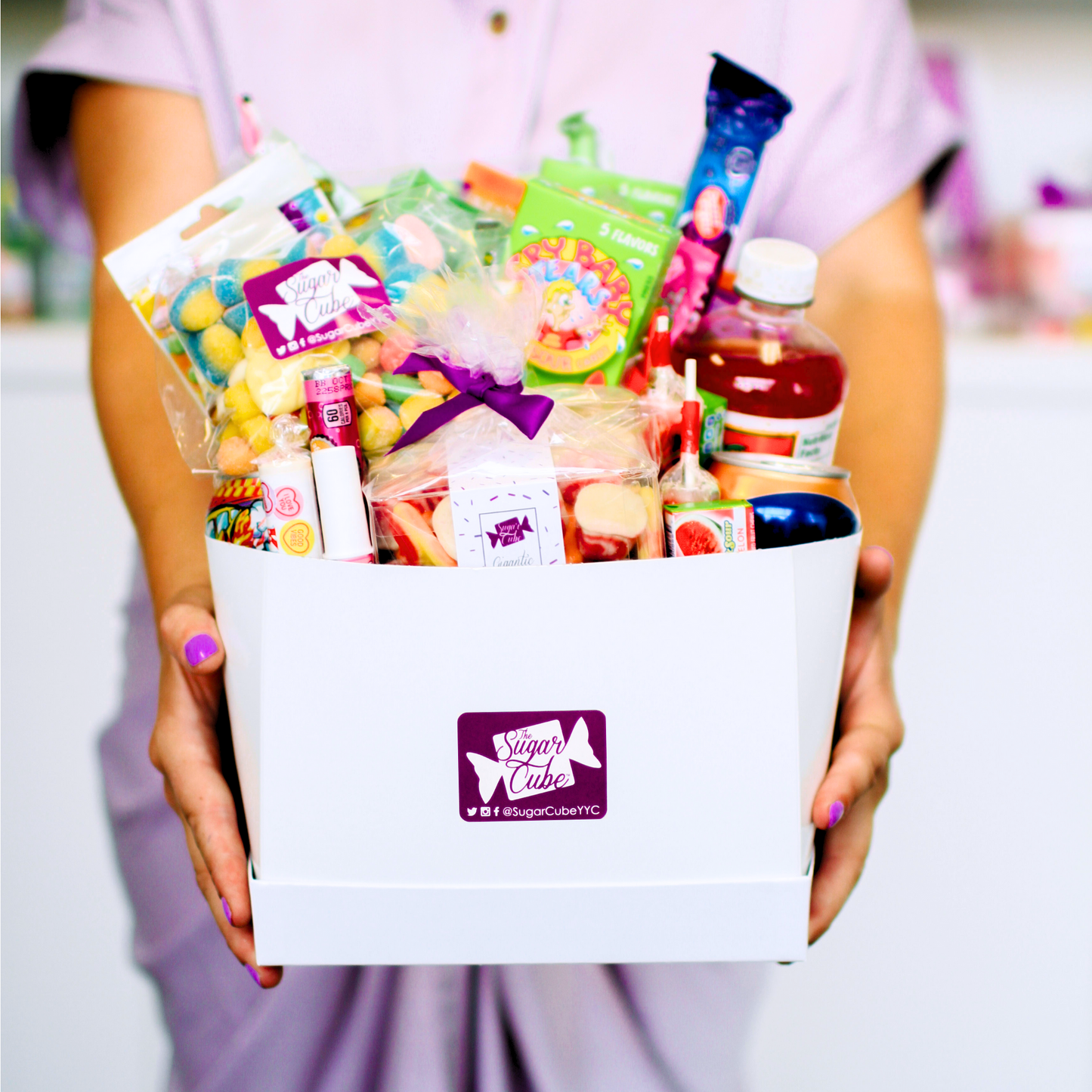Holding an Extra Large candy gift basket for size packed with approximately 40 to 50 assorted treats, including specialty soda bottles and cans