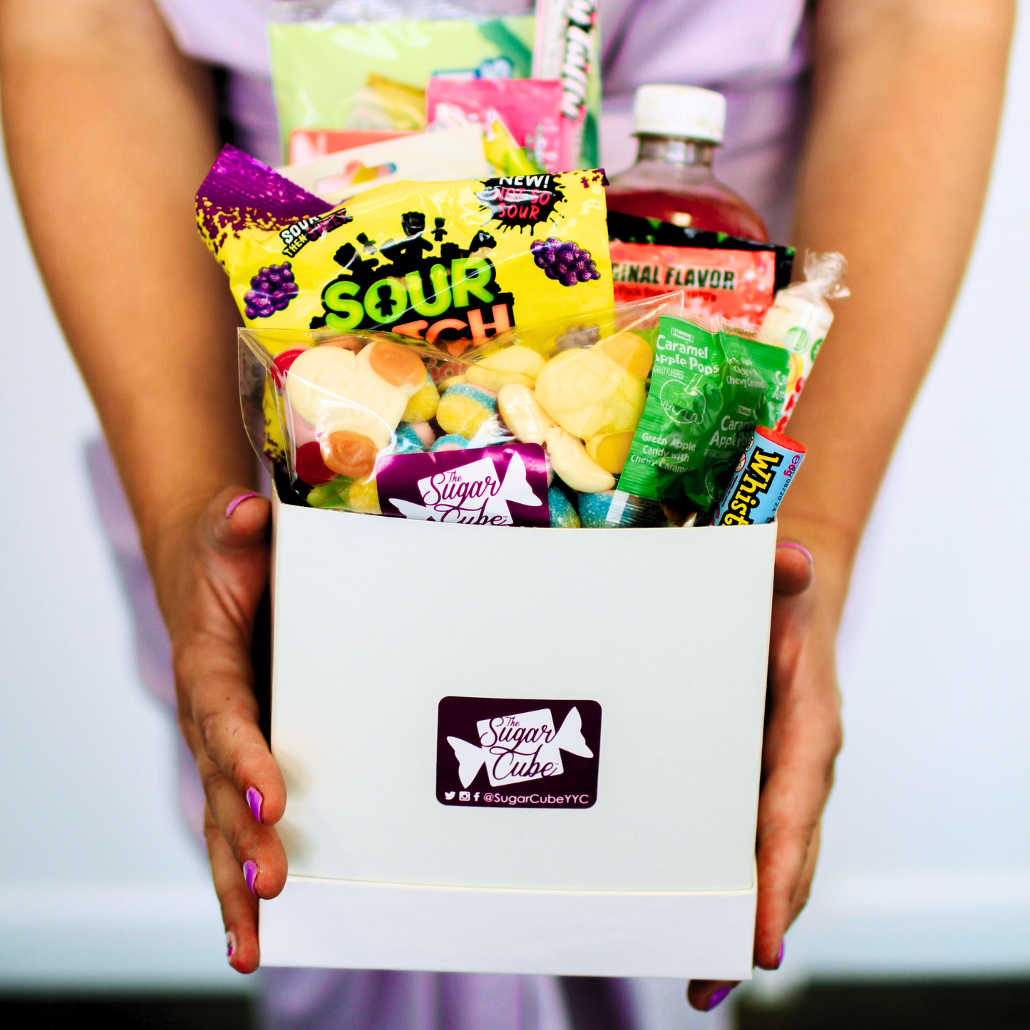 Holding a medium candy gift basket for size with approximately 10 to 15 assorted treats and a specialty soda bottle