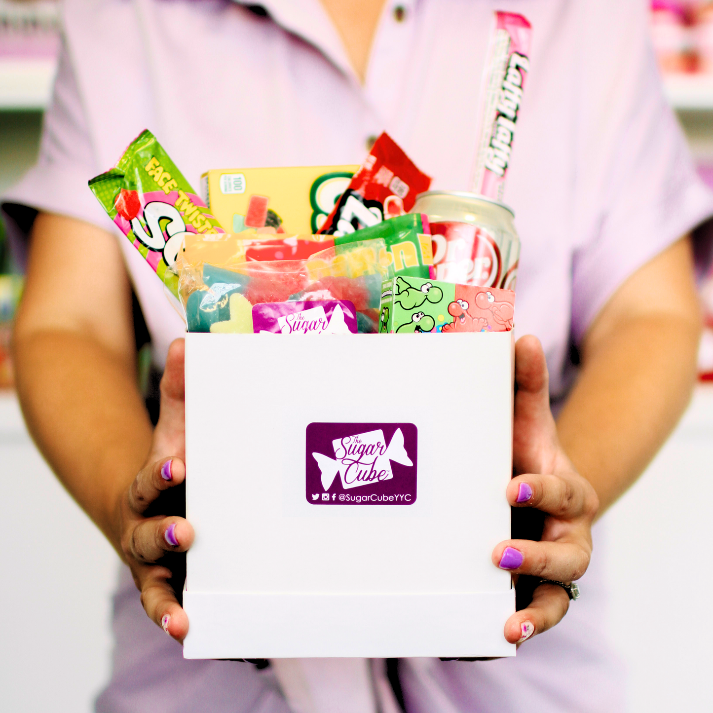 Holding a small candy gift basket for size with approximately 6 to 10 assorted treats and a specialty soda can