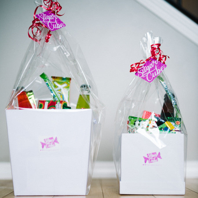 Two sizes of Christmas candy gift baskets displayed together with festive sweets, snacks and specialty drinks