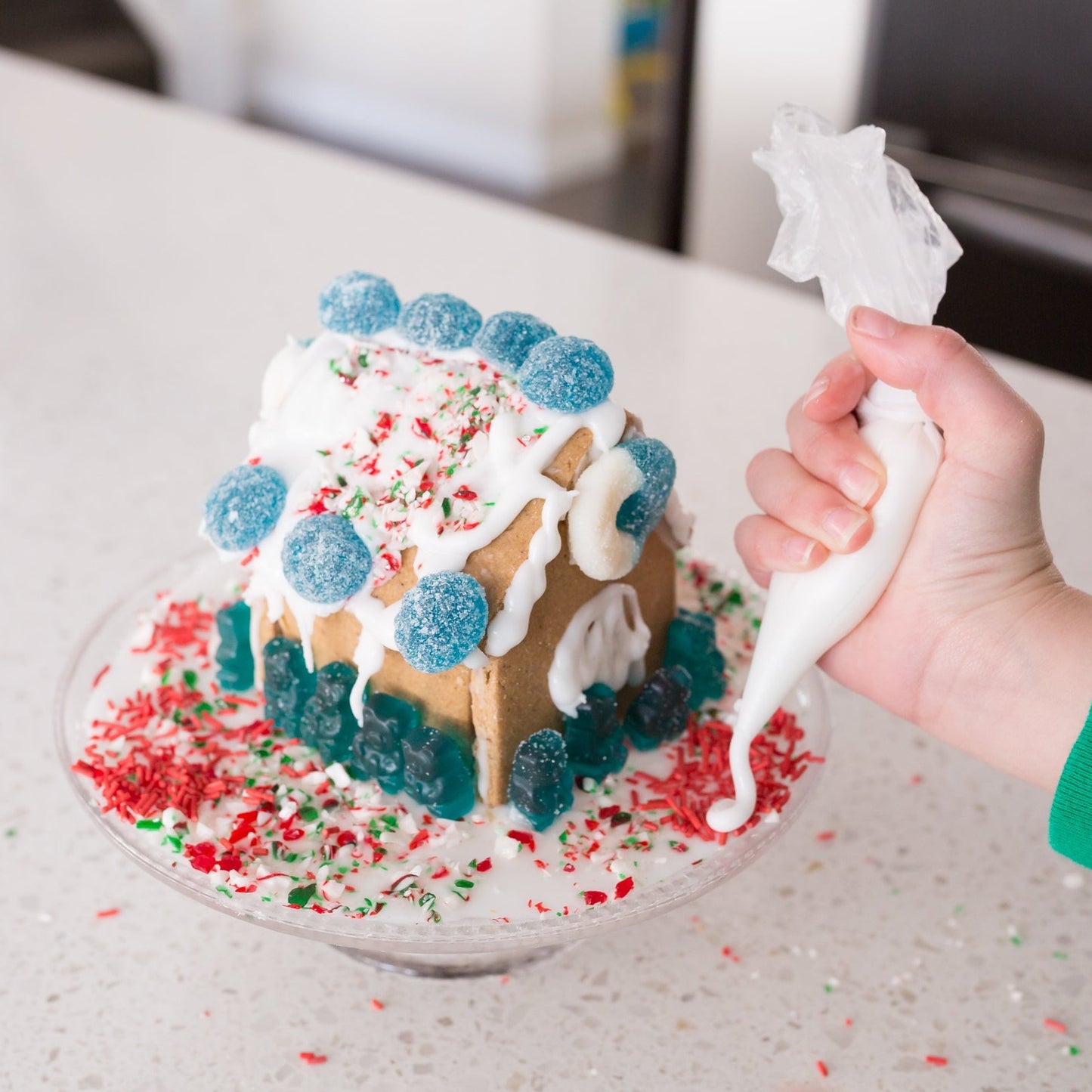 Assembled Christmas gingerbread house being decorated by hand with piped icing and festive candy